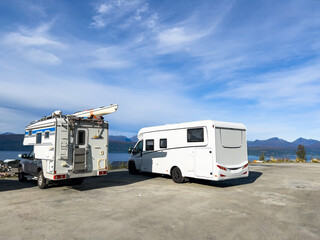 Two camper vans are parked near a scenic lake and mountain range, embodying the spirit of travel and adventure