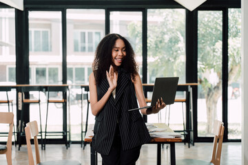 Video Call Connection: A young, enthusiastic woman connects with someone on a video call using her laptop in a modern office environment. - Powered by Adobe