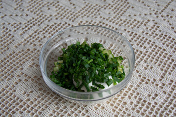 Salad of green onions and fresh cucumbers in a transparent glass plate on a table covered with a milky tablecloth