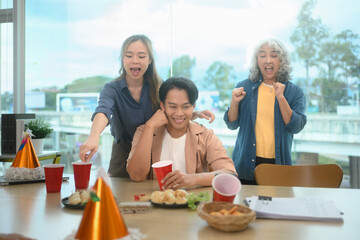 Cheerful group of colleagues enjoying snacks and drinks during a lively office party