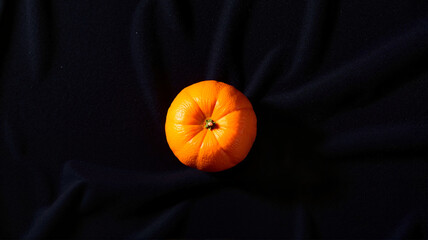 Single vibrant orange fruit on a soft black fabric background