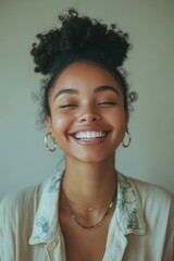 Woman with a smile on her face is wearing a necklace and earrings. She is wearing a white shirt and has her hair in a bun