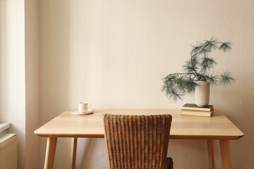 Christmas breakfast still life. Minimal winter composition. White cup of coffee, tea, plate. Pine tree branches in vase, old books on wooden table with rattan chair. Elegant Scandinavian living room.