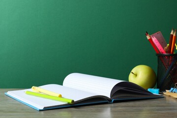 Back to school. Close-up of colorful stationery, textbooks, green apple on green chalkboard