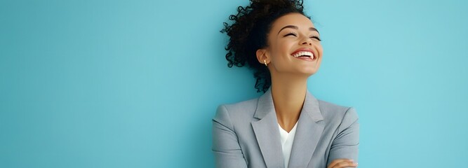 A young adult woman in a tailored gray office suit, smiling with her arms crossed on a light blue background with expansive open space around her.