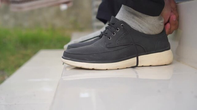 Close up of male hands tying shoelaces at home. Young man in gray pants tying shoelaces of white canvas shoe on granite floor
