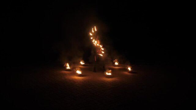 A circus woman with burning torches in her hands on a black background, the performance of artists with fire. A woman holds torches with fire and rotates them in a circle.