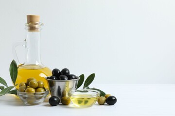 Bottle of fresh olive oil and olives with leaves on the table