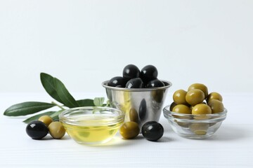 Bowl of fresh olive oil and olives with leaves on the table