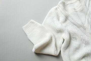 White knitted sweater on paper color background top view copy space. Texture of woolen cotton winter autumn cozy sweater, clothes. Knitted jumper, pullover, fashion. Sweater close-up