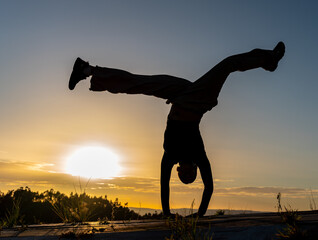 Backlit silhouette of a woman doing a face-down breakdance pirouette at sunset © jcasorey