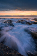 Water flows into the rocky channel on the coastline.