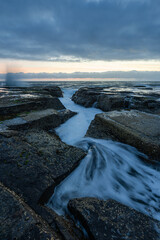 Water flows into the rocky channel on the coastline.