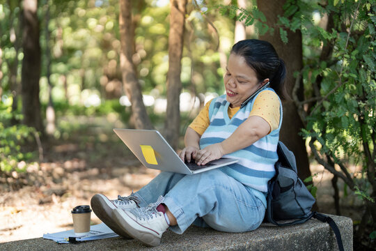 Woman with dwarfism multitasking with laptop and phone in park