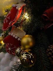 A beautifully decorated Christmas tree at night. The tree is adorned with various festive ornaments, including red mittens with white snowflakes, golden baubles, pine cones, and white fluffy decoratio