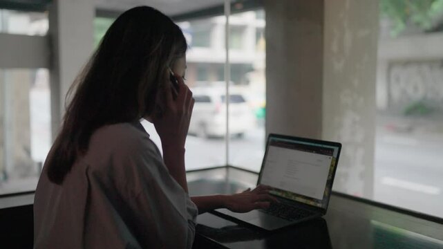 Woman engrossed in work, multitasks on her laptop and phone, showcasing dedication and efficiency in a modern setting. 