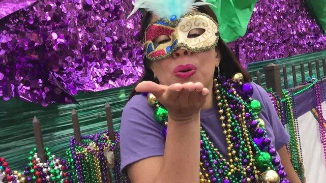 A young latin tourist female, wearing mask, costumes and necklaces celebrating Mardi Gras through the streets while taking a selfie with her cellphone in New Orleans, USA