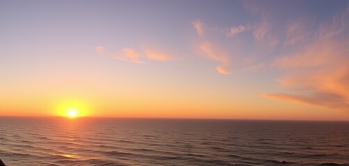 Fototapeta premium A breathtaking panoramic view of a golden sunset over a calm ocean, with soft waves reflecting hues of orange, pink, and purple
