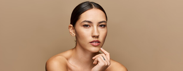 A young beautiful woman with brunette hair reflects thoughtfully against a neutral backdrop.
