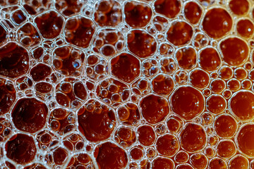 Intricate pattern of bubbles in a dark, reddish-brown liquid.  Close-up macro photography reveals a...