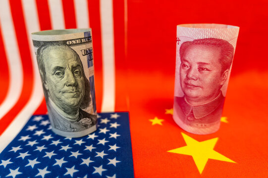 USA vs China trade war concept. Close up of 100 Yuan banknote and one hundred Dollar banknotes with focus on portraits of Benjamin Franklin and Mao Tse-tung against the background of national flags..