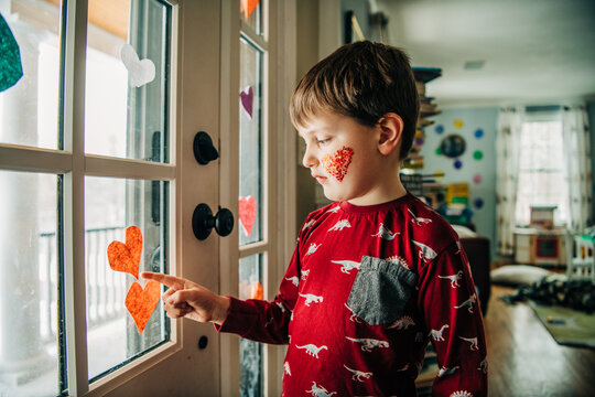 Boy in red dinosaur shirt with glitter heart touches window hearts