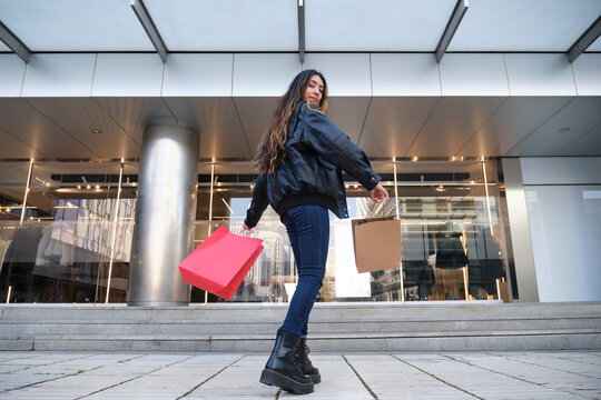 Young woman walking away from a store, looking back over her shoulder