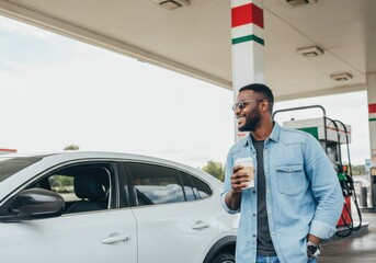 Happy man enjoying a coffee break at a gas station after filling up his car's tank