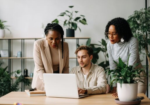 Business colleagues working together, analyzing data on a laptop in a plant-filled office