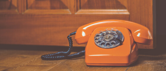 Orange rotary phone on wooden surface photographed in retro style