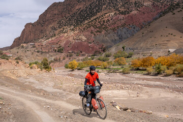Mountain bikepacking adventure. Cyclist with a bike loaded with bags smiles as he climbs a steep hill in the Atlas Mountains in Morocco.