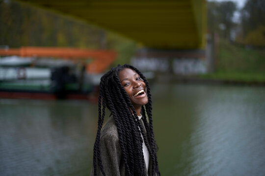 Smiling young woman with braided hair enjoying a day by the river under a bridge, Brandenburg, Germany