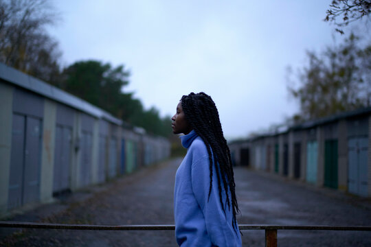Woman in a blue coat looking skywards on a cloudy day by storage units, Brandenburg, Germany