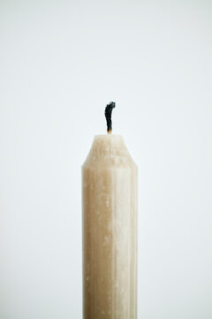 Close-up of an unlit beige candle with a burnt wick against a white background.
