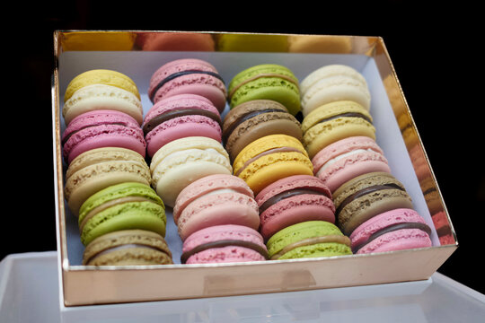 Colorful macarons arranged neatly in a golden box on a white surface.
