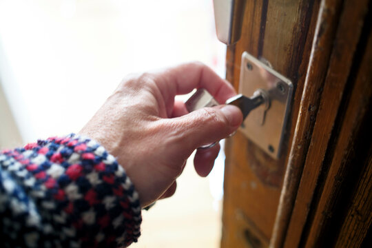 Close-up of a person's hand inserting a key into a wooden door lock.