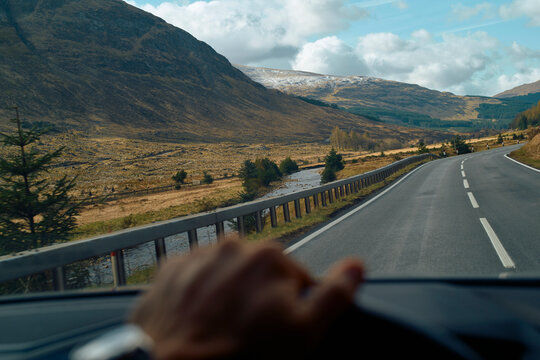 Mountain landscape viewed from a car with the driver's hand on the steering wheel, Highlands, Scotland
