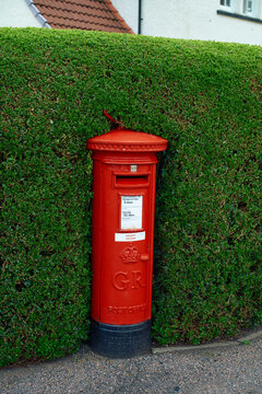 A red British post box stands embedded in a neatly trimmed green hedge, Scotland