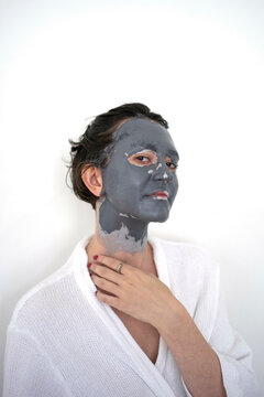 Young woman with a facial clay mask posing against a white background.