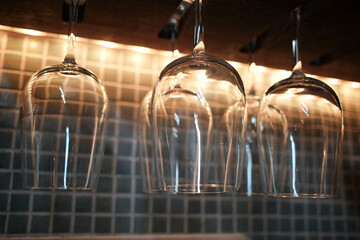 Wine glasses hanging upside down above a bar counter with a warm, dimly lit ambiance.