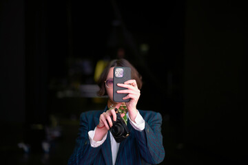 A woman with a camera takes a selfie using a smartphone, obscuring their face.