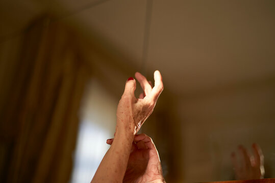 Graceful woman's hands with red nail polish are poised above a wooden bed frame in a sunlit room, Rome, Italy