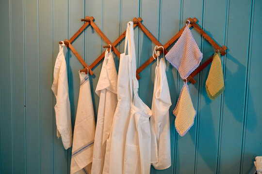 Chef's aprons and dish towels hanging on wooden hooks against a blue paneled wall, Trondheim, Norway