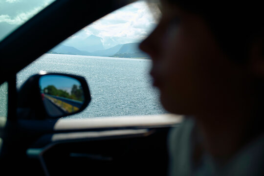 Silhouette of a person in a car with a scenic fjord view and mountains in the background, Trollstiege, Trollvegen, Norway