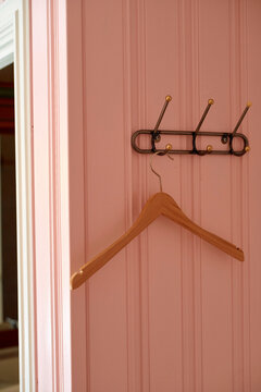A single wooden hanger hangs on a minimalistic metal hook against a pink striped wall, Norway