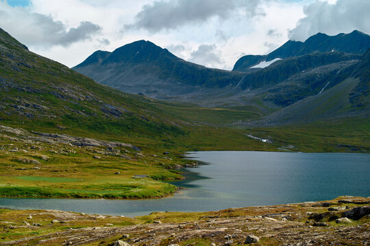 A serene mountain landscape featuring a calm lake in the foreground and rocky mountains in the background, Trollstiege, Trollvegen, Norway