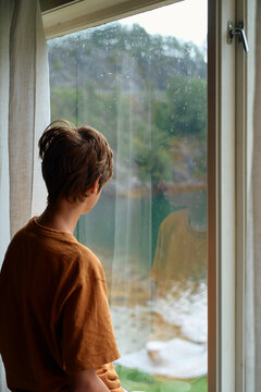 Young boy gazing out of a rain-splattered window on a gloomy day, Geirangerfjord, Norway