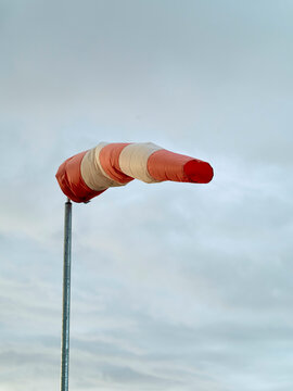 A red and white windsock fully extended against a cloudy sky, indicating strong wind conditions, Norway