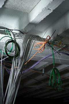 Multicolored network cables hanging from a metal tray on a concrete ceiling in a technical environment.