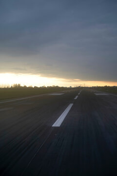 An empty runway during sunrise with clouds in the sky creating a dramatic backdrop